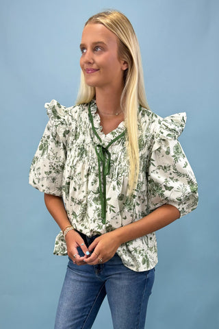 Woman wearing a floral blouse with ruffled sleeves against a blue background