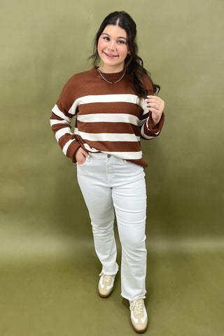Woman wearing a brown and white striped sweater with white pants against a green background