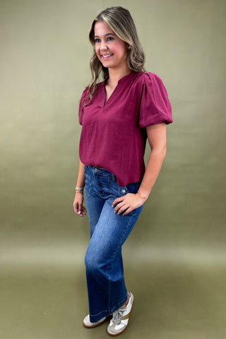 Woman wearing a magenta top and blue jeans against a green background