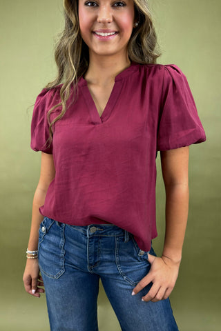Woman wearing a maroon top and blue jeans against a green background