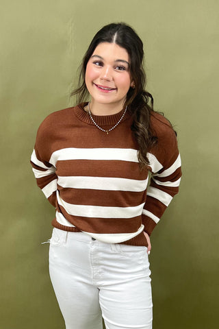 Person wearing a brown and white striped sweater with white pants against a green background