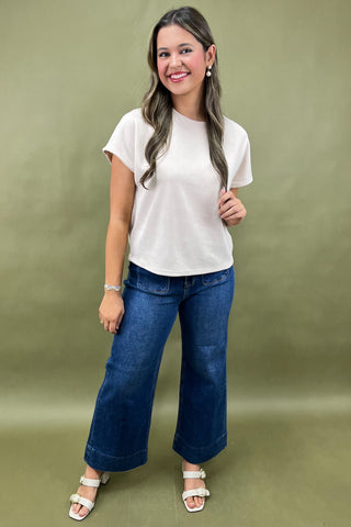 Woman wearing a white t-shirt and blue jeans against a green background