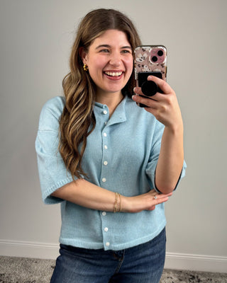 Woman taking a mirror selfie wearing a light blue shirt and jeans.