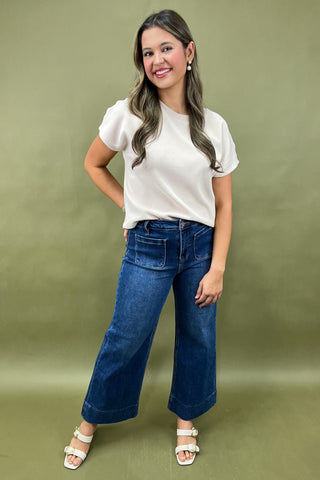 Woman wearing a white top and blue jeans against a green background