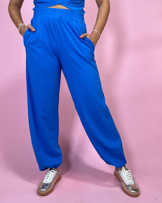 Person wearing blue high-waisted pants and white sneakers on a pink background