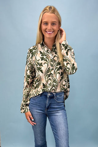 Woman wearing a patterned blouse and blue jeans against a light blue background