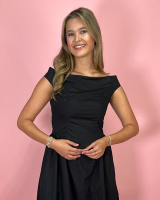 Woman wearing a black off-shoulder dress against a pink background