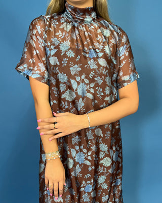 A woman wearing a sheer brown high-neck dress with a light blue and white floral pattern