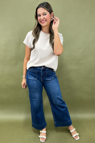 Woman wearing a white t-shirt and blue jeans against a green background