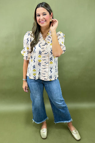 Woman wearing a patterned blouse and blue jeans against a green background