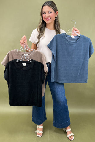 Woman holding three shirts on hangers against a green background