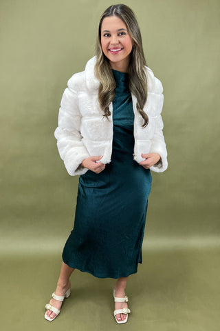 Woman wearing a white puffer jacket over a teal dress on a green background