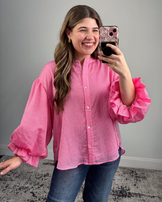 Woman wearing a pink ruffled blouse taking a mirror selfie.