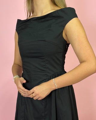 Black off-shoulder dress worn by a person on a pink background