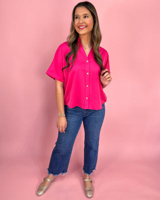 Woman wearing a bright pink blouse and blue jeans against a pink background