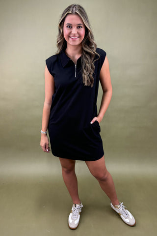 Woman wearing a black sleeveless dress with a collar on a beige background