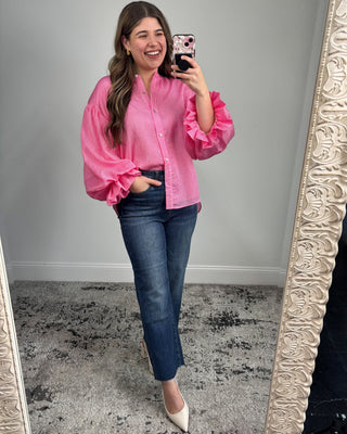 Woman taking a mirror selfie wearing a pink blouse and blue jeans.