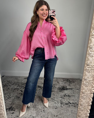Woman taking a mirror selfie wearing a pink blouse and blue jeans.
