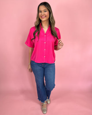 Woman wearing a bright pink blouse and blue jeans against a pink background