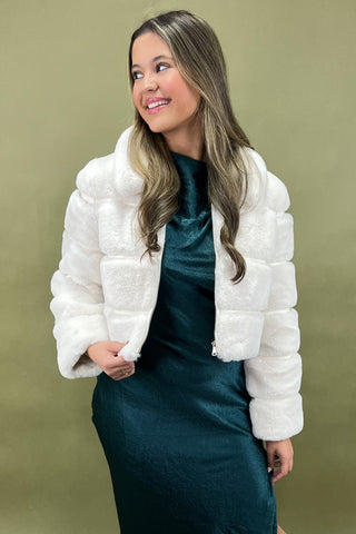 Woman wearing a white puffer jacket over a teal dress on a green background