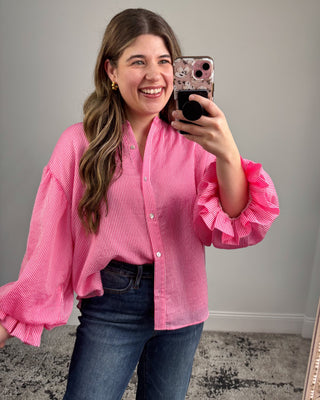 Woman taking a mirror selfie wearing a pink blouse with ruffled sleeves.