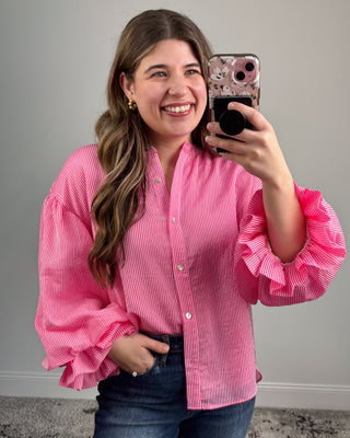 Woman taking a mirror selfie wearing a pink ruffled blouse against a gray background