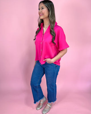 Woman wearing a bright pink blouse and blue jeans against a pink background
