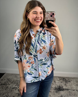 Woman taking a mirror selfie wearing a floral shirt and jeans.