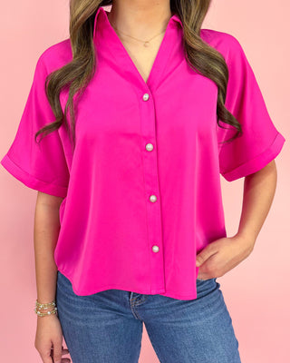 Person wearing a bright pink button-up shirt with a plain background