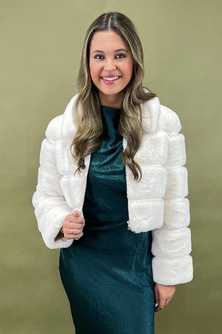 Woman wearing a white puffer jacket over a teal dress on a green background