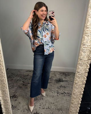 Woman taking a mirror selfie wearing a floral blouse and blue jeans.