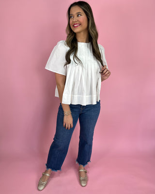 Woman wearing a white blouse and blue jeans against a pink background