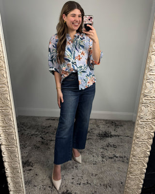 Woman taking a mirror selfie wearing a floral blouse and blue jeans.