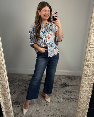 Woman taking a mirror selfie wearing a floral blouse and blue jeans.