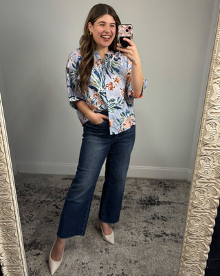 Woman taking a mirror selfie wearing a floral blouse and blue jeans.