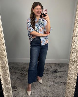 Woman taking a mirror selfie wearing a floral blouse and blue jeans.