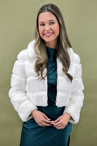 Woman wearing a white puffer jacket over a teal dress against a green background
