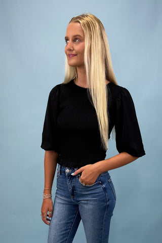 Woman wearing a black top and blue jeans against a light blue background