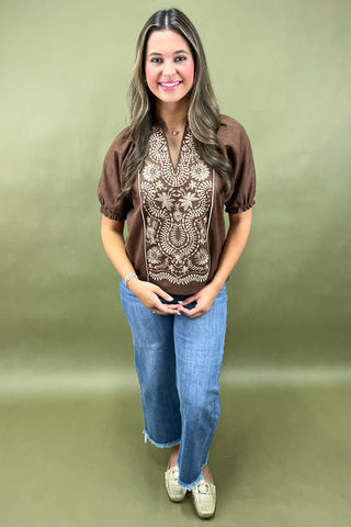 Woman wearing a brown blouse with lace details and blue jeans on a green background
