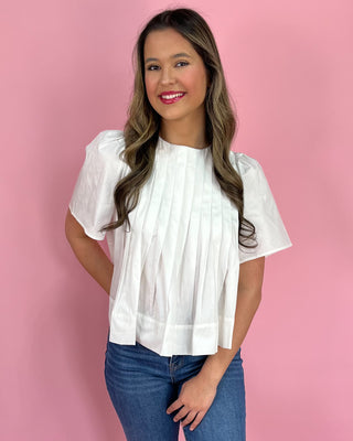 Woman wearing a white blouse and blue jeans against a pink background