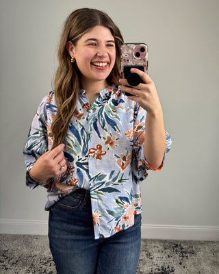 Woman taking a mirror selfie wearing a floral shirt and jeans.