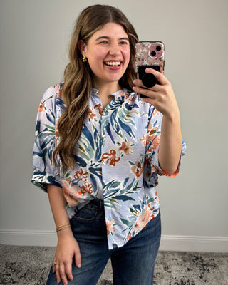 Woman taking a mirror selfie wearing a floral shirt and jeans.