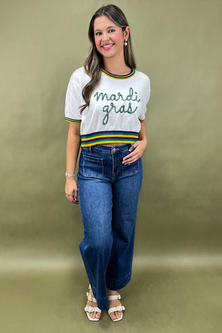 Woman wearing a 'mardi gras' themed shirt and blue jeans on a gold background