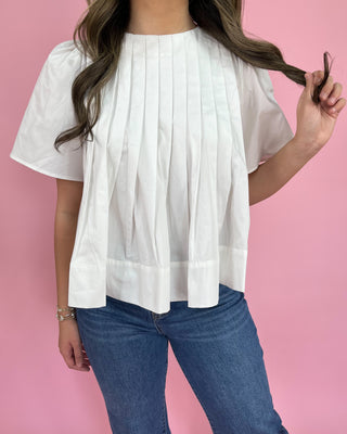 Person wearing a white blouse and blue jeans against a pink background