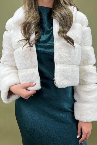 White fur jacket worn over a teal dress on a plain background
