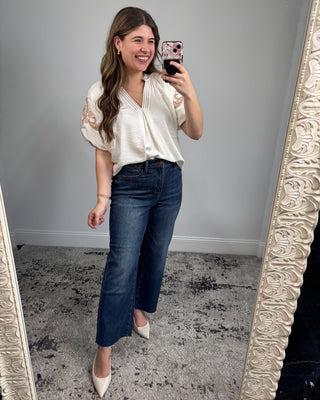 Woman taking a mirror selfie wearing a white blouse and blue jeans.