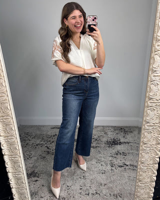 Woman taking a mirror selfie wearing a white blouse and blue jeans.