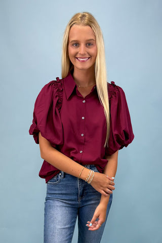 Woman wearing a burgundy blouse with puff sleeves against a light blue background