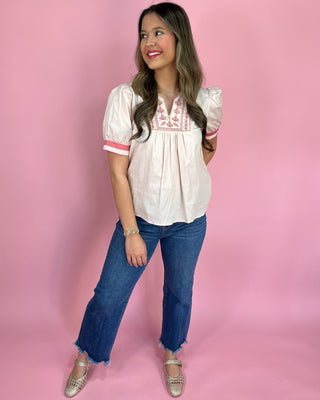 Woman wearing a white blouse with pink trim and blue jeans on a pink background