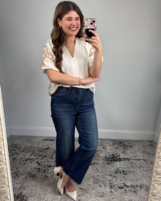 Woman taking a mirror selfie wearing a white blouse and blue jeans.